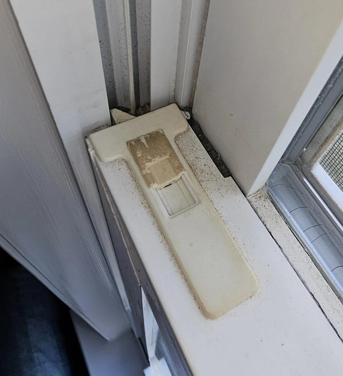 Close-up of a worn tilt latch on a white window sash.