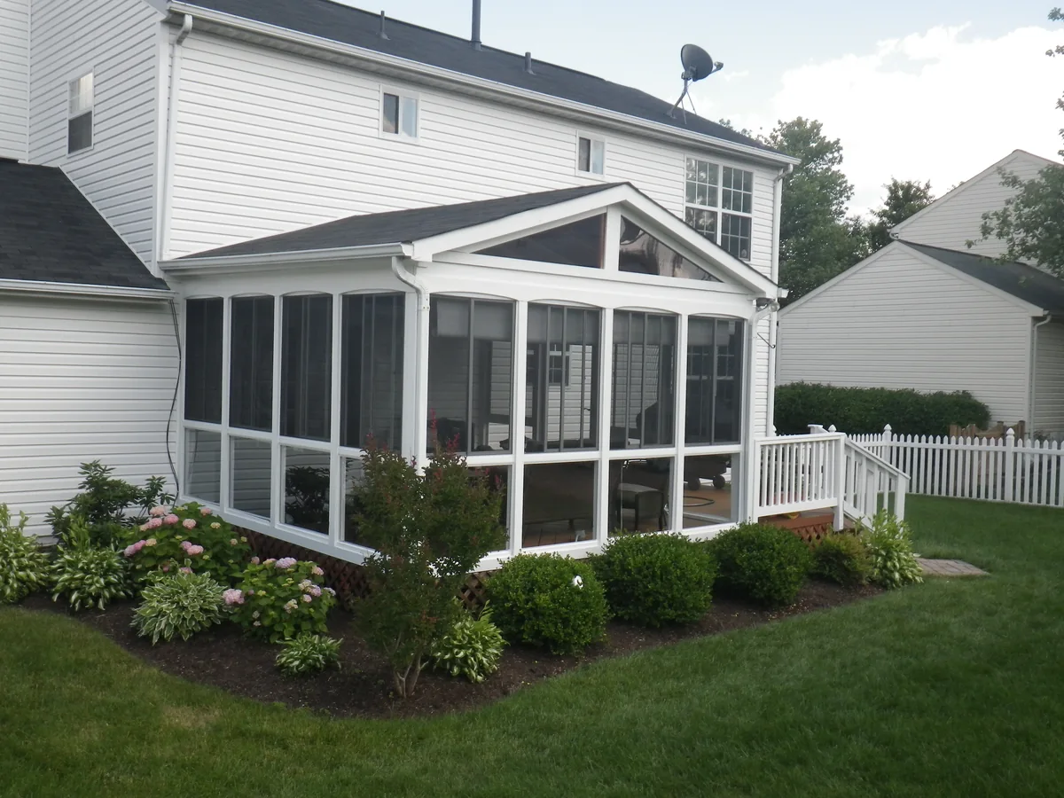 White-framed gabled screened porch beside a landscaped lawn