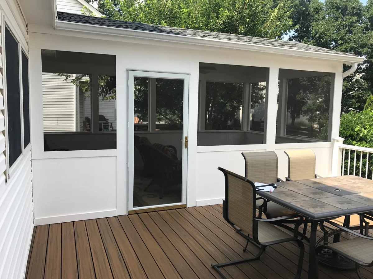 White porch enclosure and screen door opening onto a furnished wood deck.