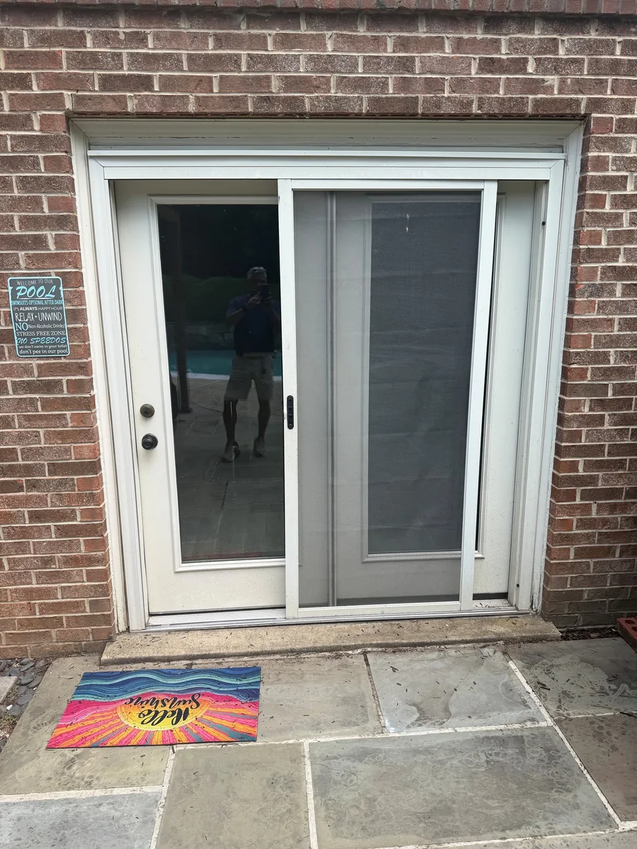 White sliding patio screen door beside a glass door in a brick wall