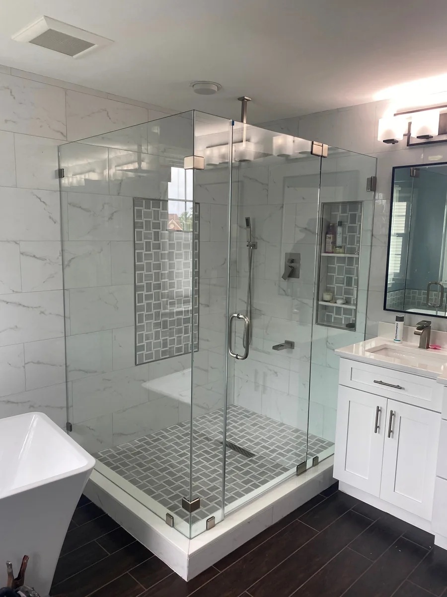 Frameless corner shower enclosure with chrome hardware, pale marble-look tile, and geometric tile accents.
