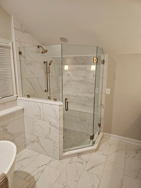 A clear corner shower enclosure has gold-tone hardware.