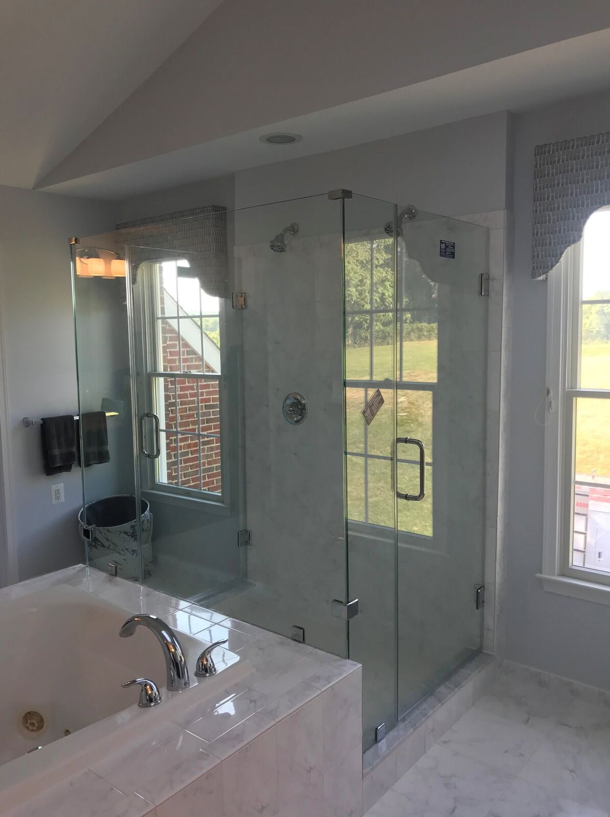 A frameless 90-degree corner shower beside a soaking tub under a window
