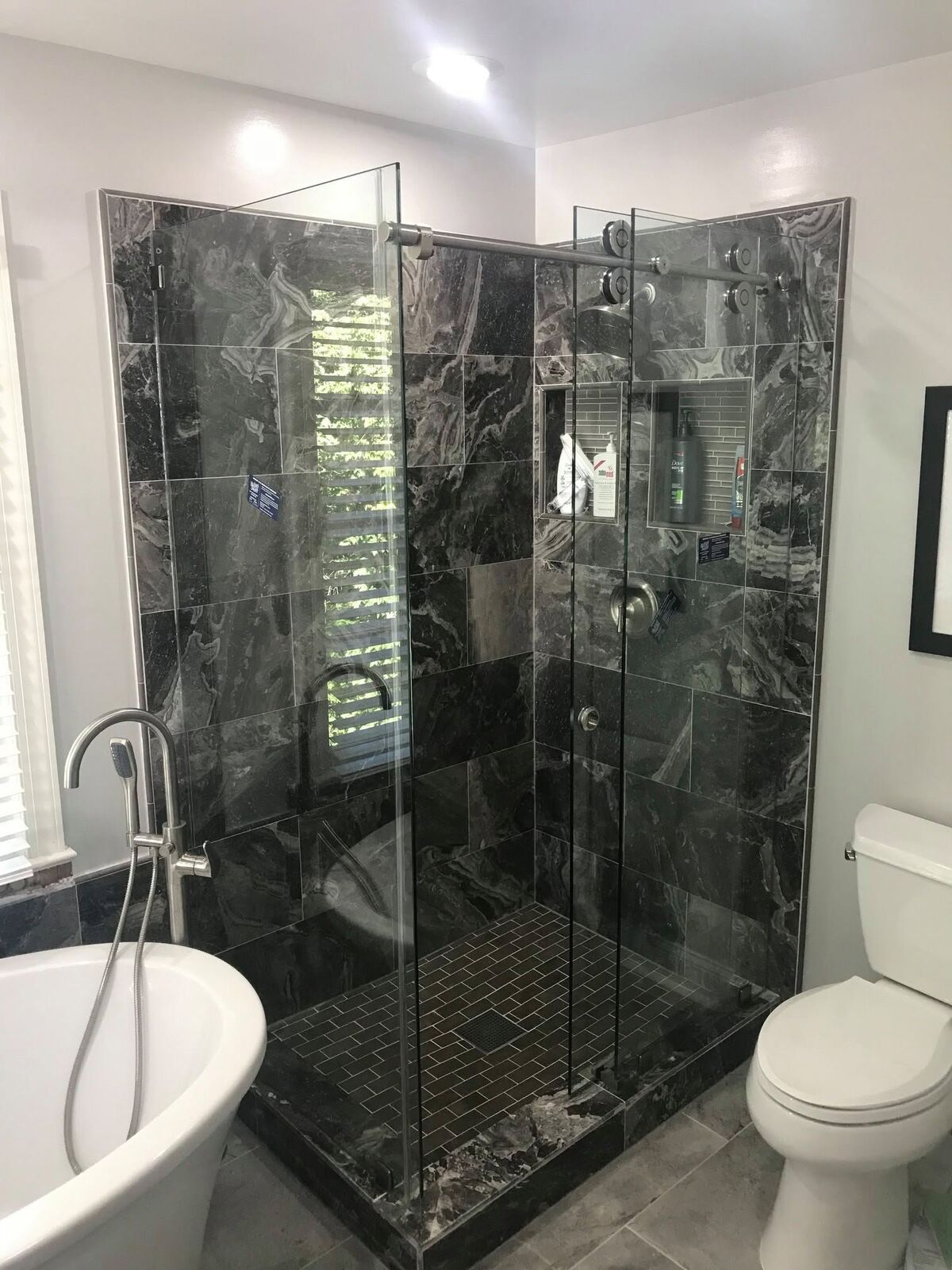 A glass shower with brushed-nickel sliding rollers and rail against dark tile