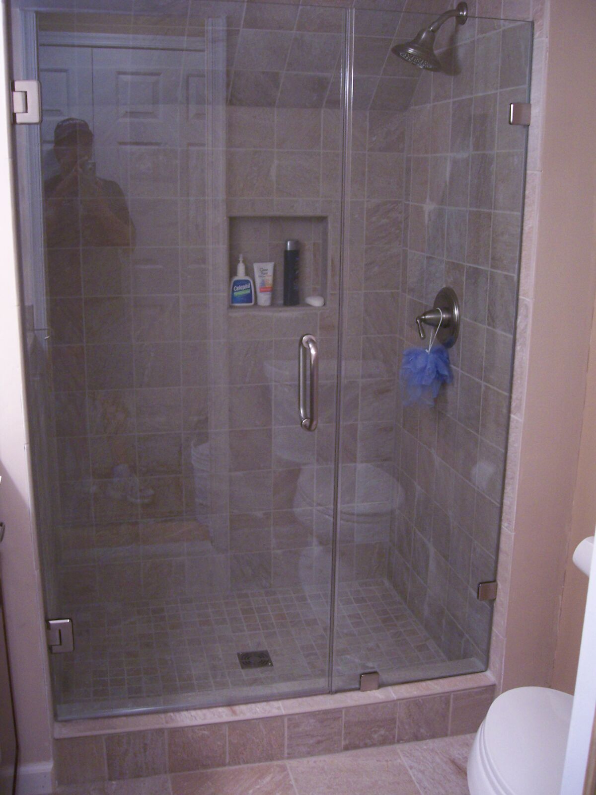 An inline glass shower enclosure with gray tile and a recessed niche