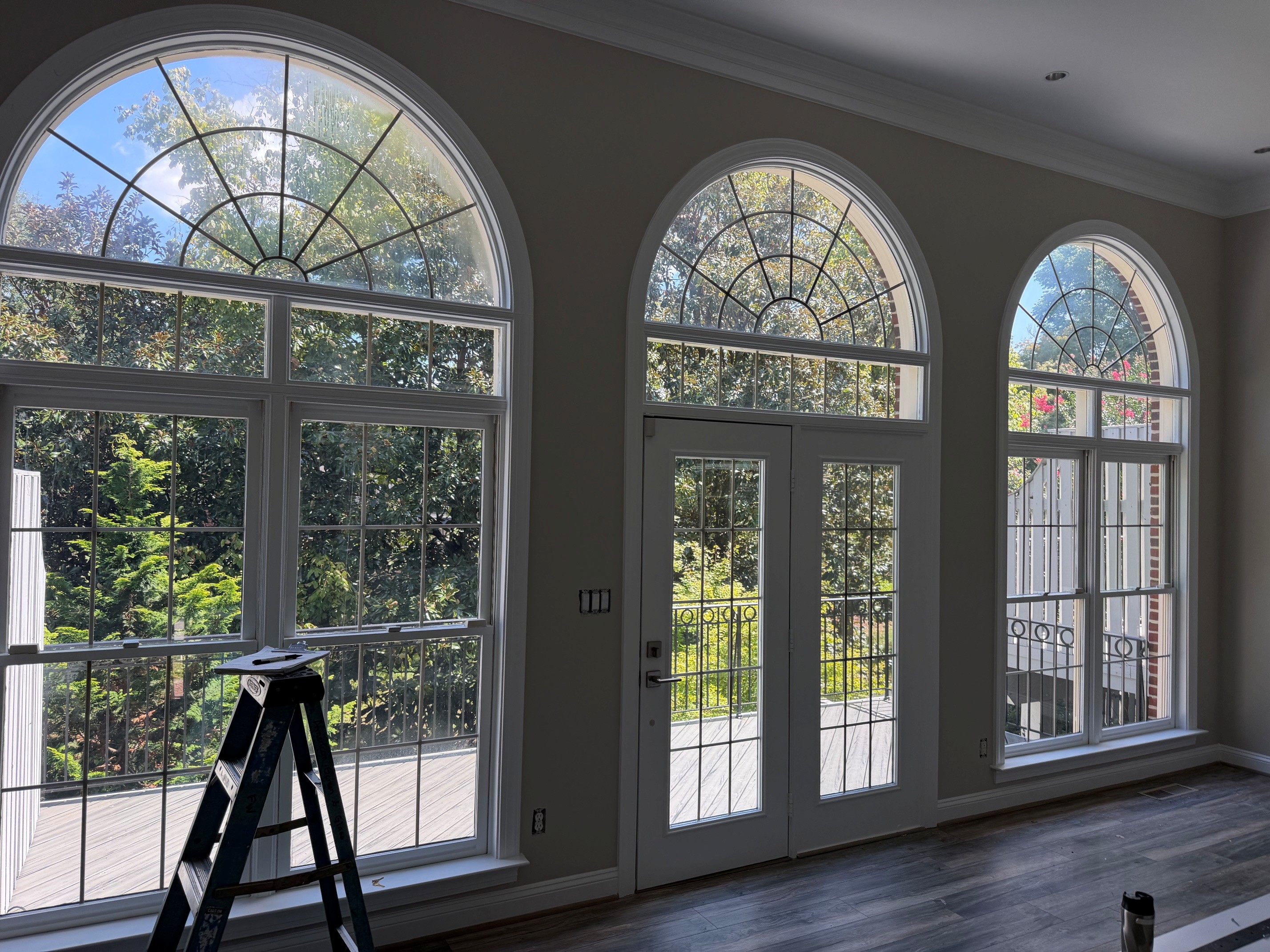 A tall arched window wall and glazed doors overlooking a garden