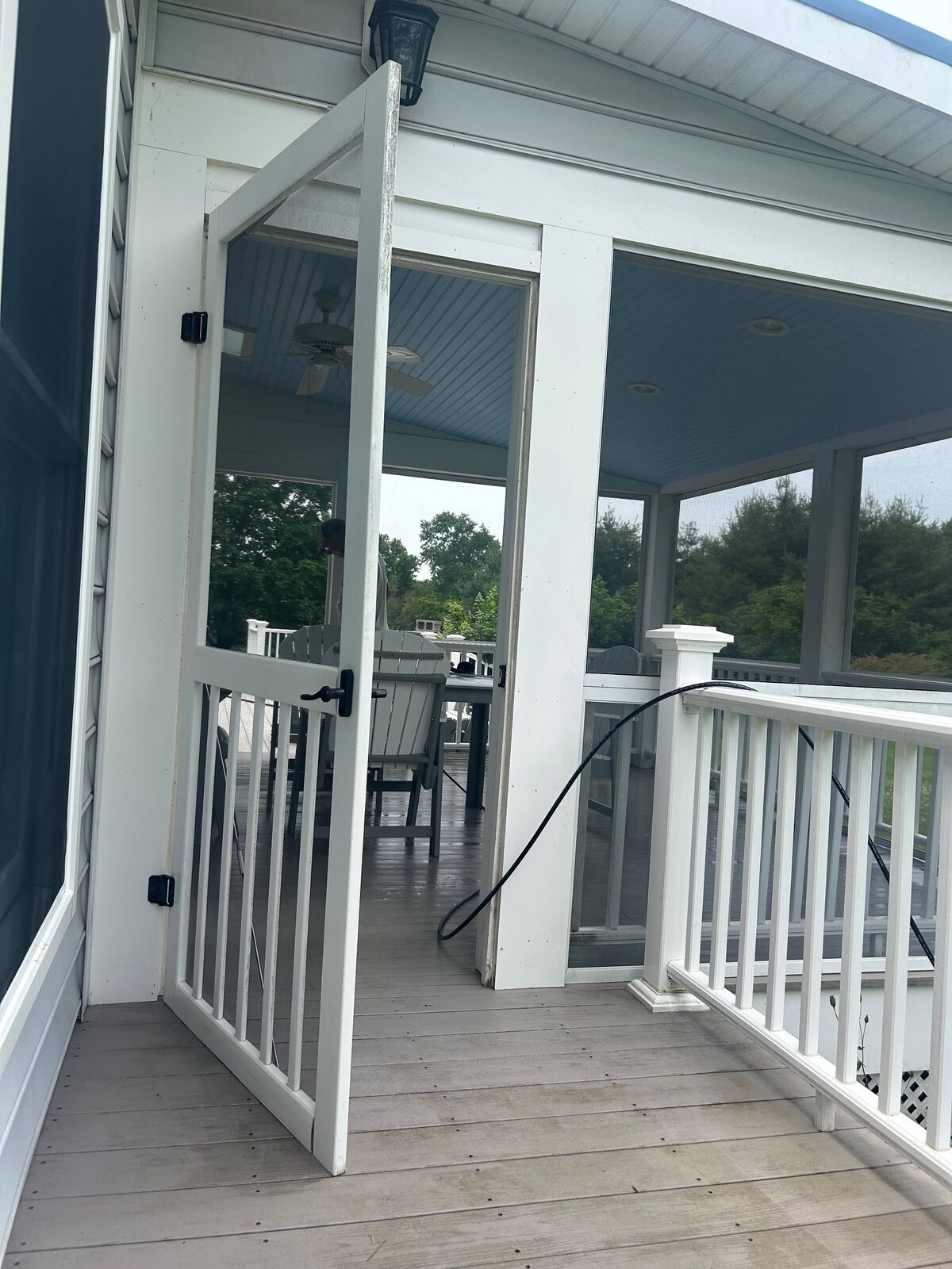 A white porch screen door standing open onto a screened porch deck