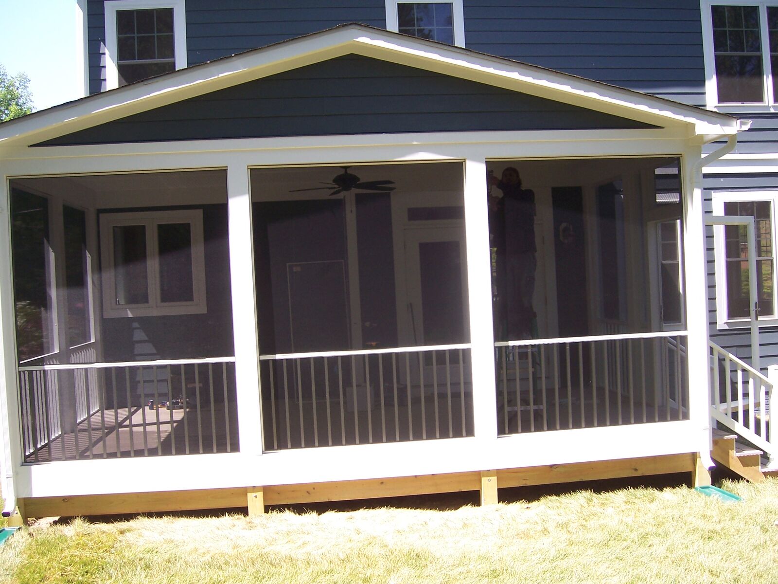 A wide gabled screened porch with dark screen panels and white trim