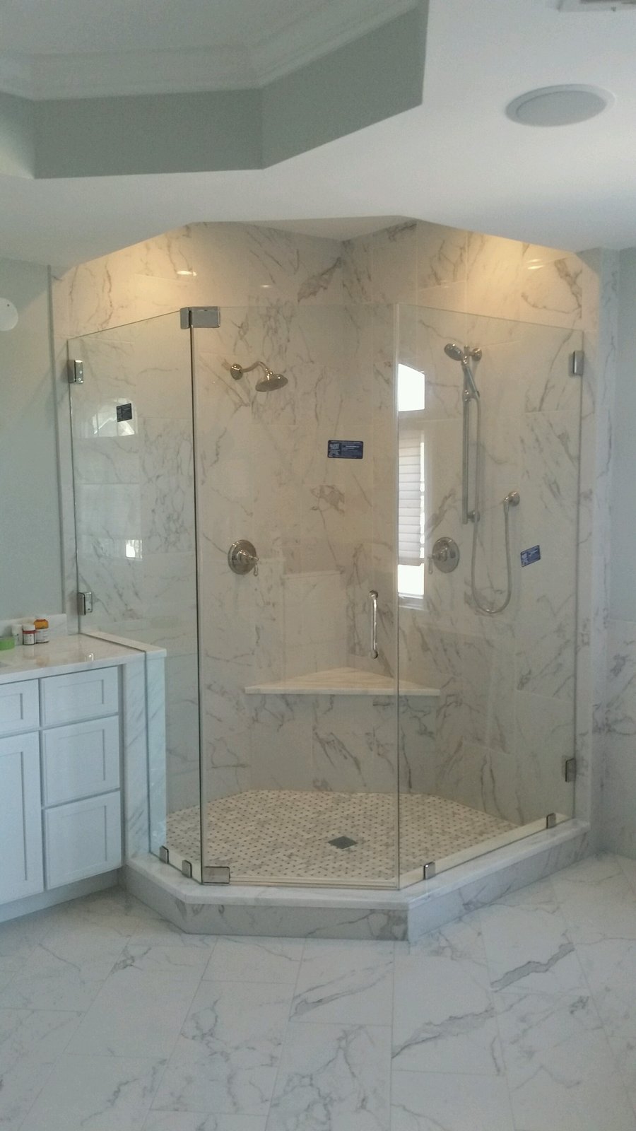 A frameless neo-angle glass shower enclosure with marble-look tile and a corner seat