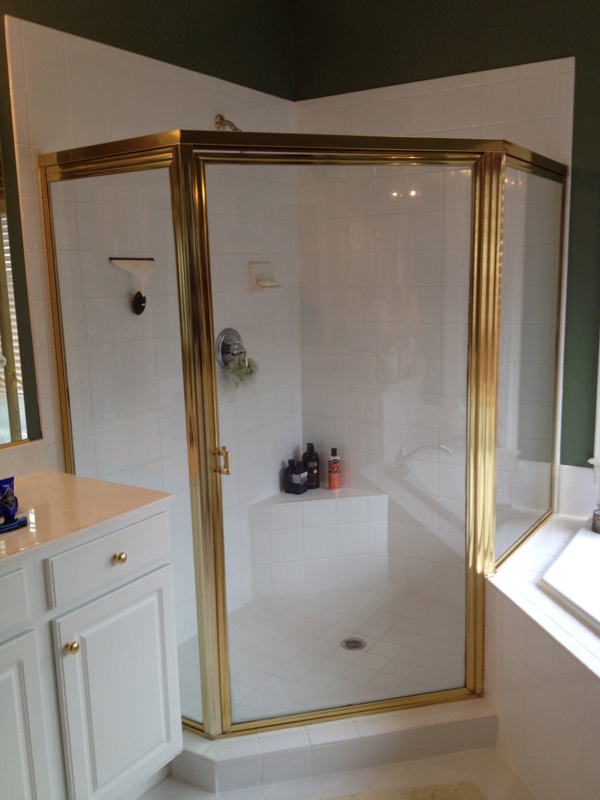 An older brass-tone framed neo-angle shower enclosure on a white-tiled curb