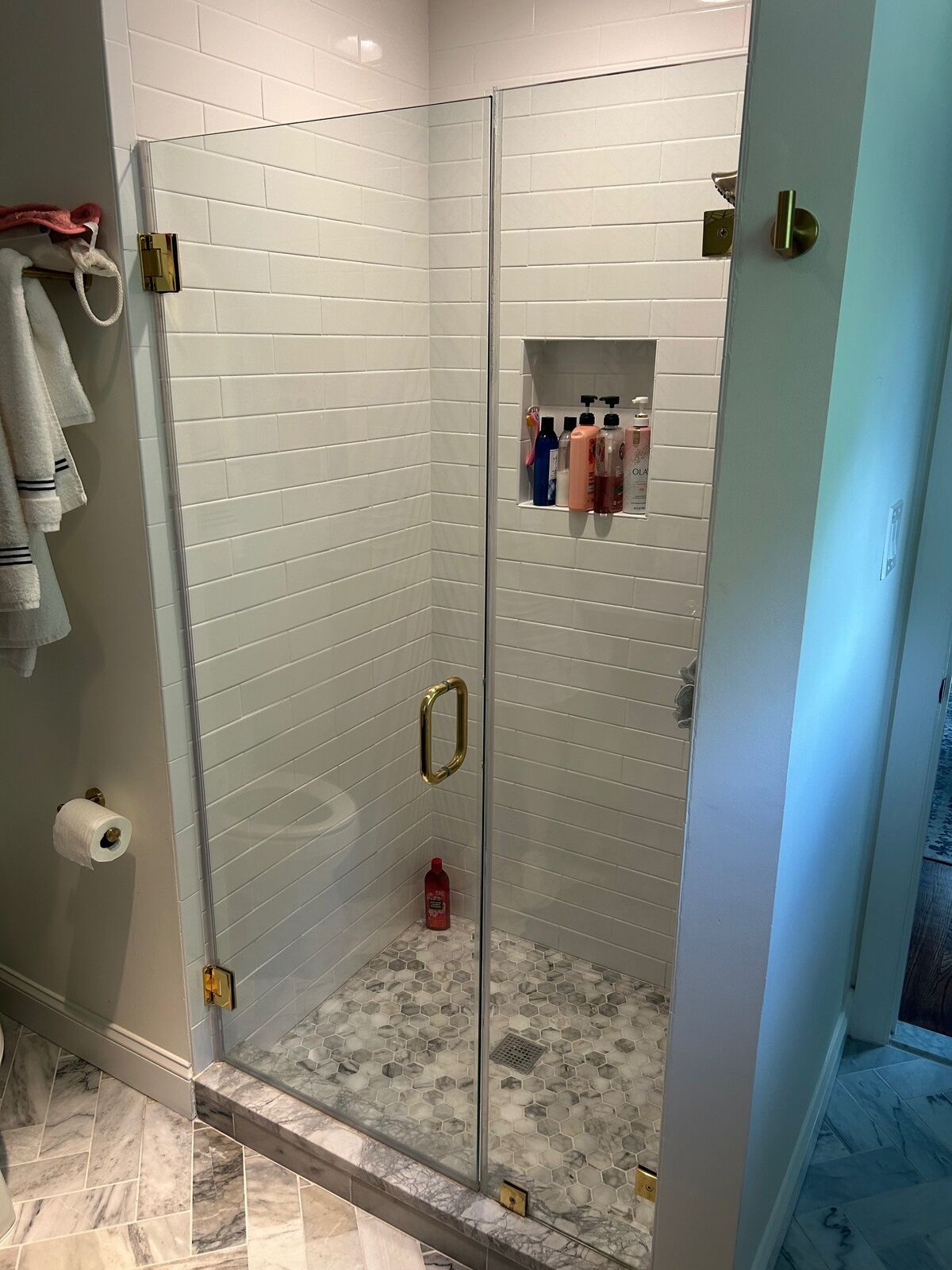 A frameless shower door with brass-tone hinges and handle