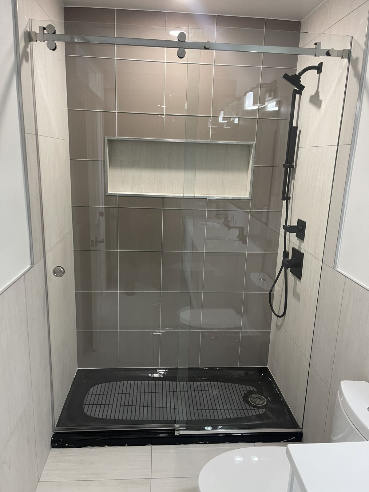 A sliding glass shower door with a black base in a gray tiled shower