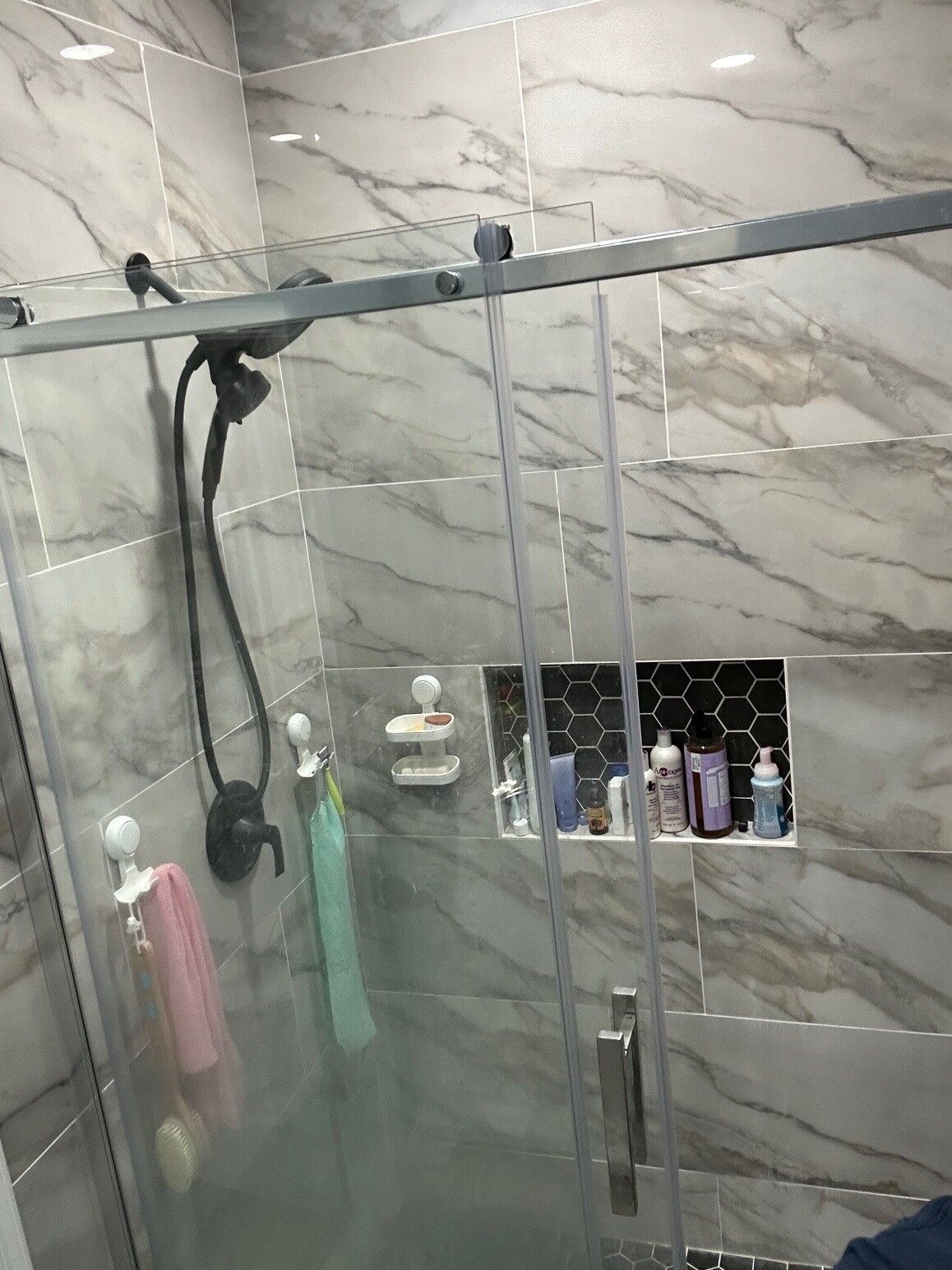 A sliding glass shower door on a top rail with marble-look tile and a hexagon mosaic niche