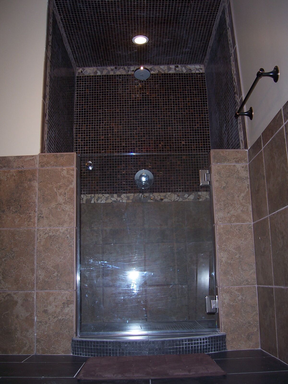A full-height glass steam shower door closing to a dark mosaic-tiled ceiling with tan tile walls
